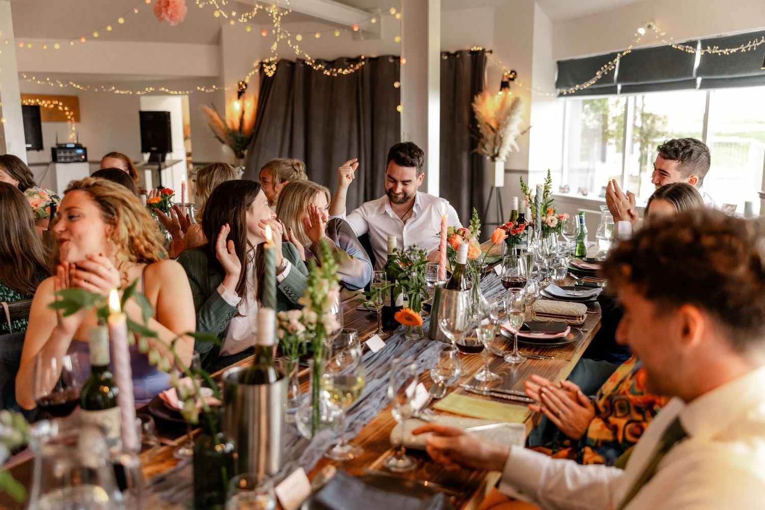 Wedding reception guests enjoying a lively dinner celebration with string lights and decorations.
