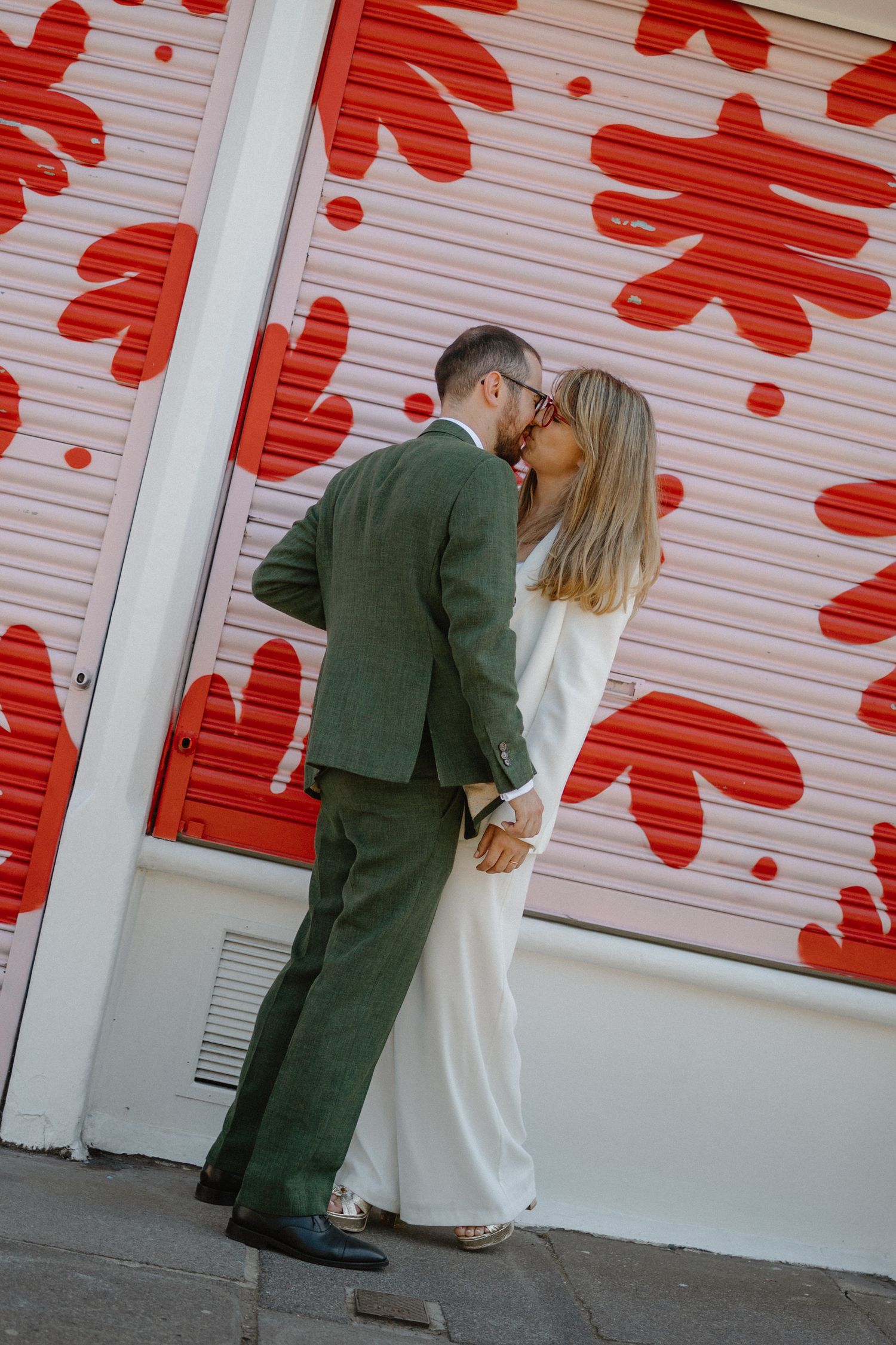 A couple performs a romantic dip pose against a wall with red flower designs.
