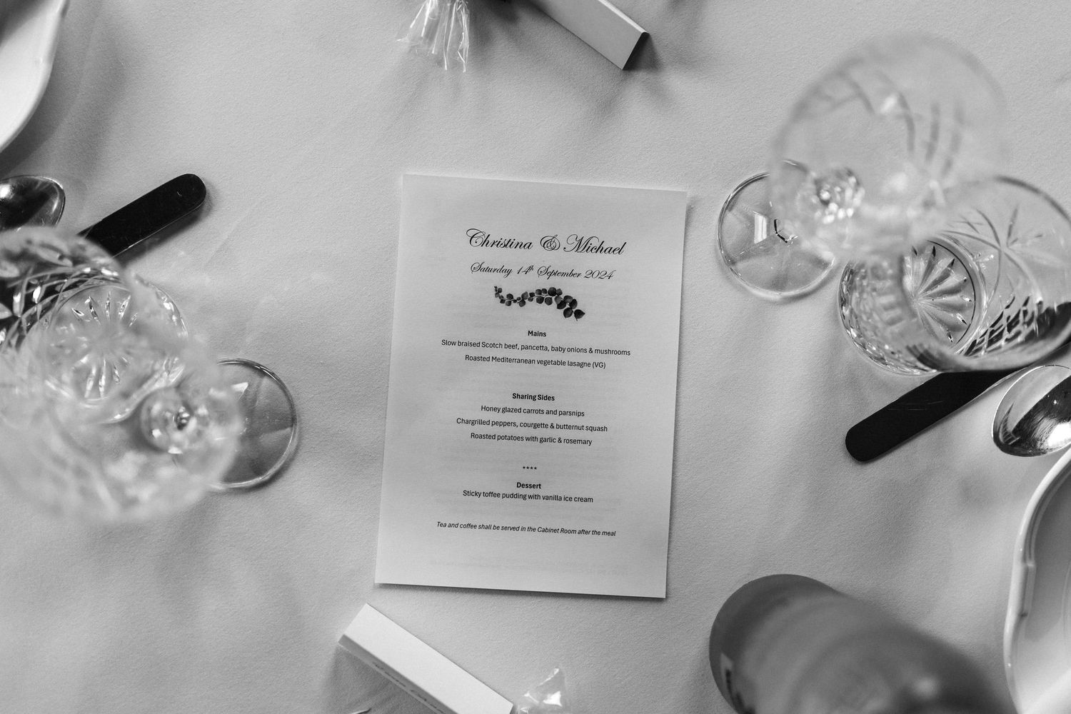 Wedding reception place settings with menus and wine glasses on elegant white tablecloths.