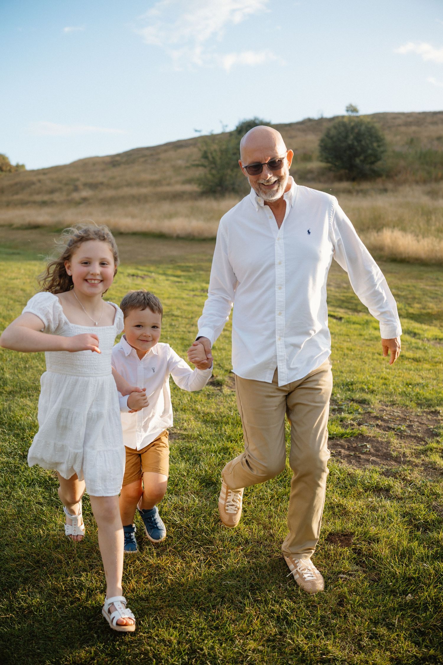 Family running and playing together on green hillside during outdoor photo session.