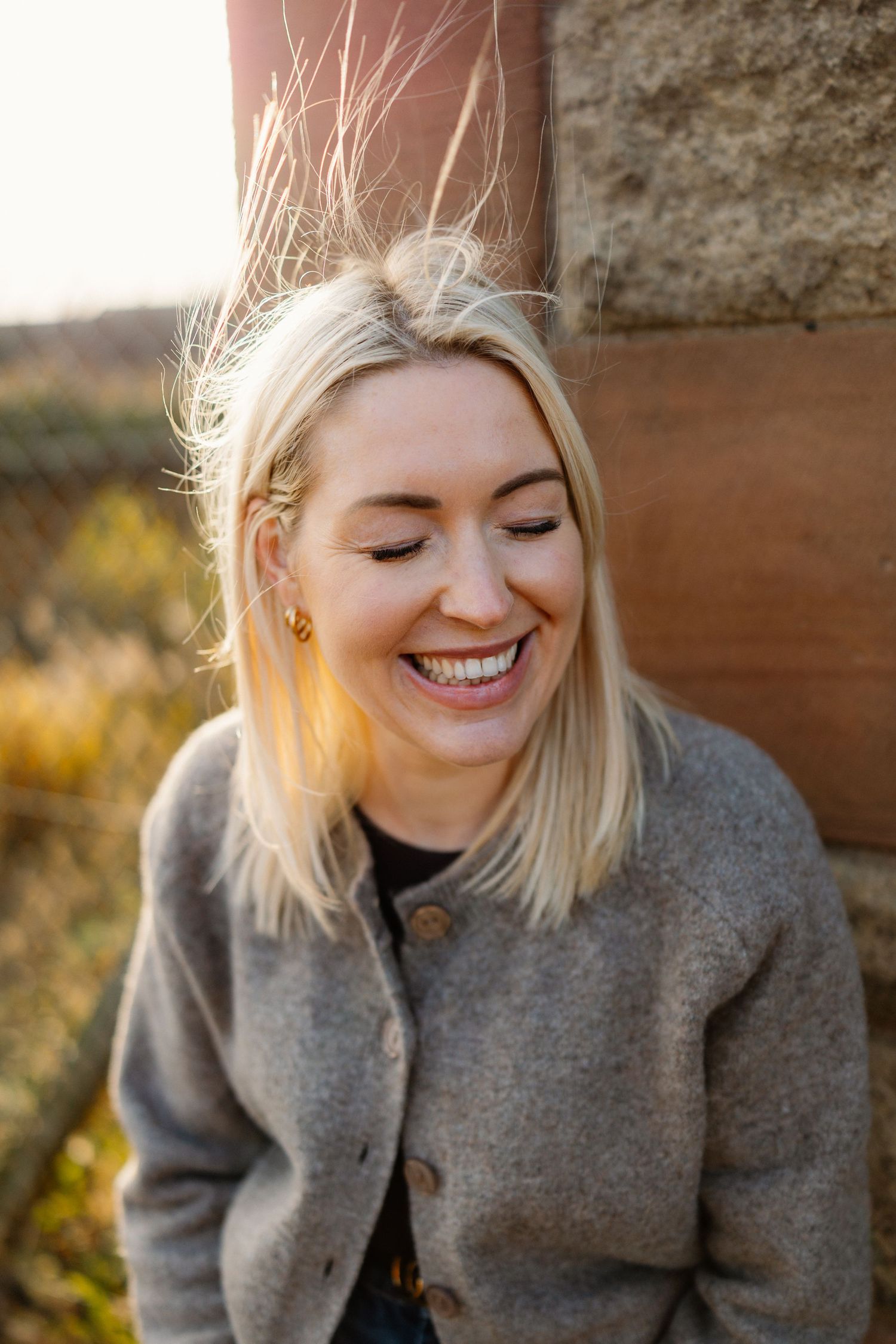 Person in cozy grey sweater smiling warmly in golden hour light.