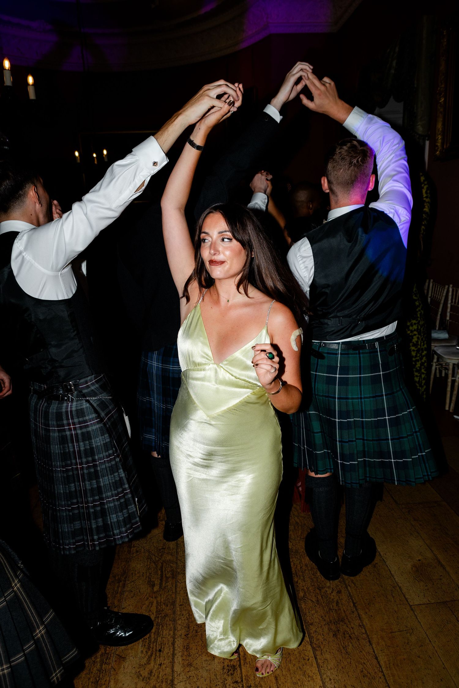 Wedding reception dancers in traditional kilts move across a dimly lit dance floor.