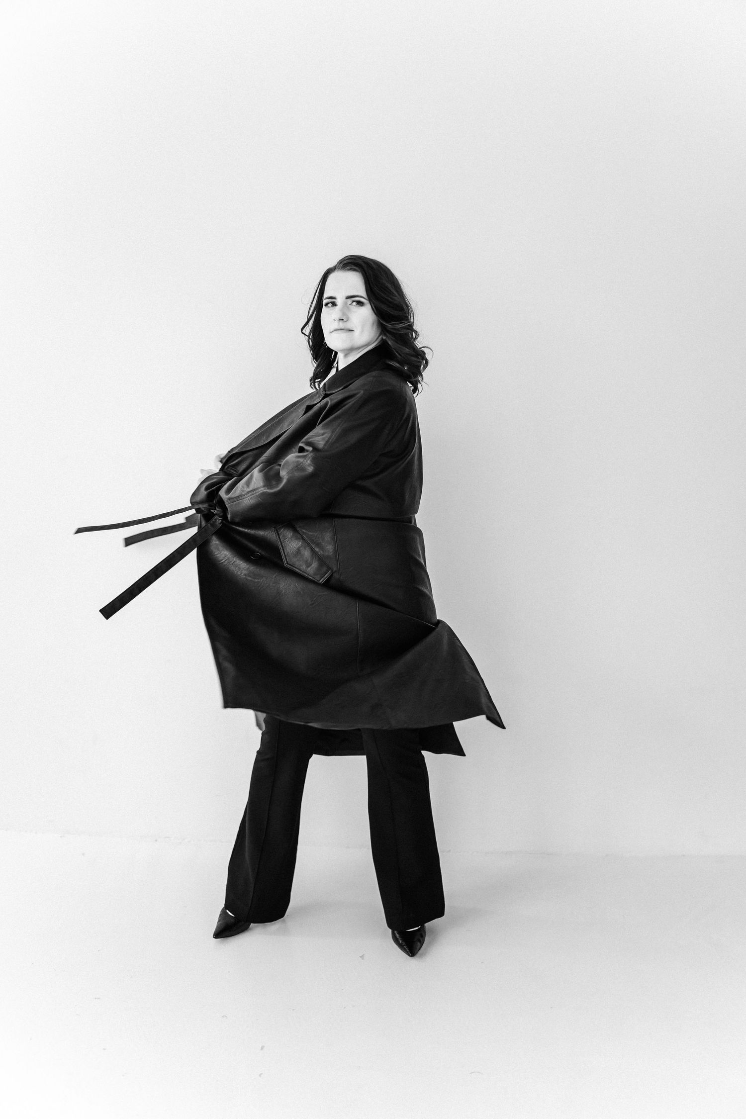 Dramatic fashion poses in black coat against minimalist white studio background.
