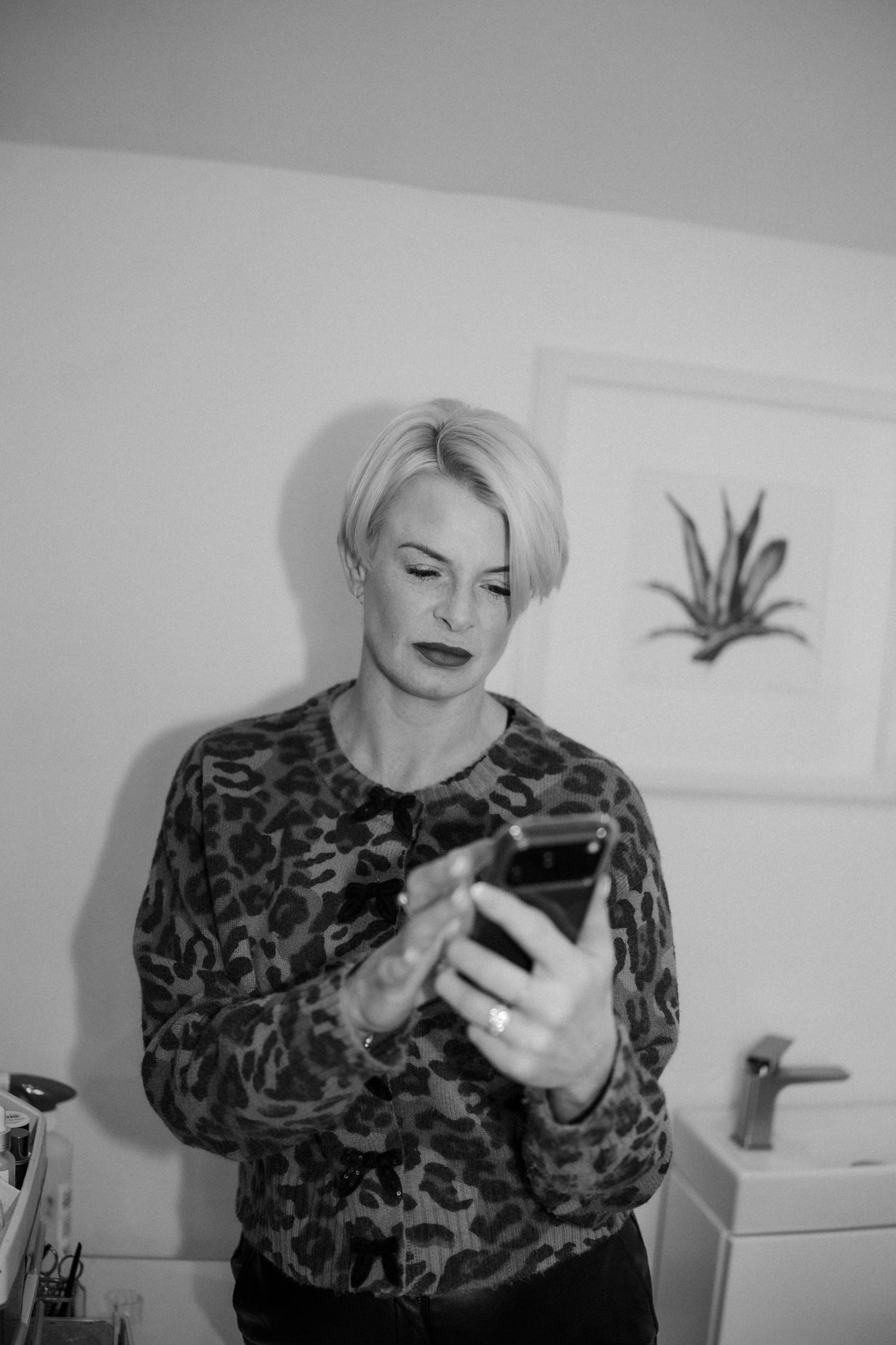 Person in leopard print top looking at and scrolling through mobile phone while sitting indoors.