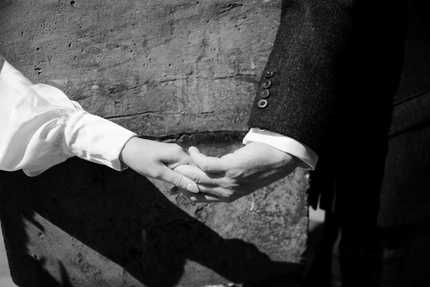 Black and white photo of a couple holding hands, one in a white shirt and the other in a dark suit jacket.