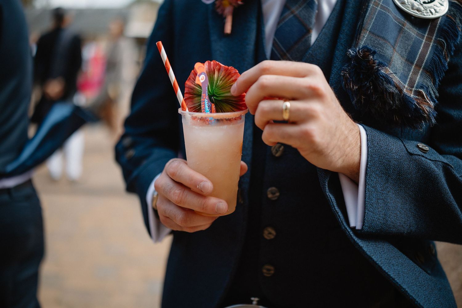 Groom holding a pink strawberry cocktail with a striped straw at a Scottish wedding reception.