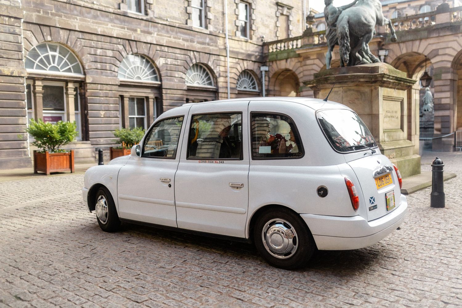 White classic London taxi cab parked on cobblestone street outside historic stone building.