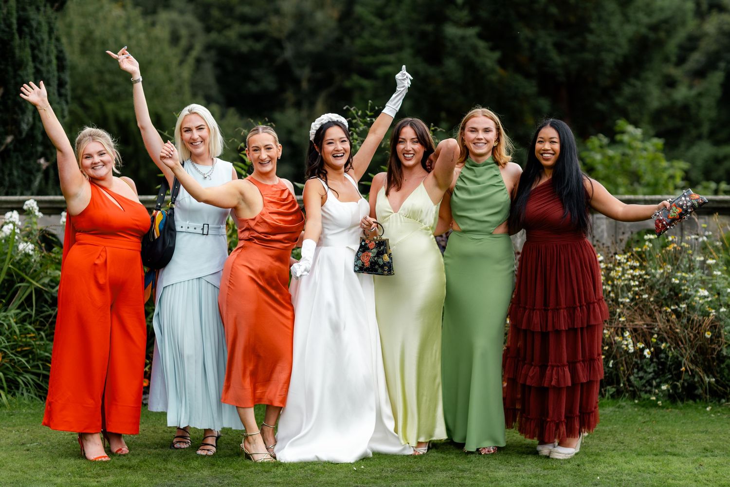 Bride posing with six bridesmaids in colorful dresses, celebrating outdoors at a garden wedding.