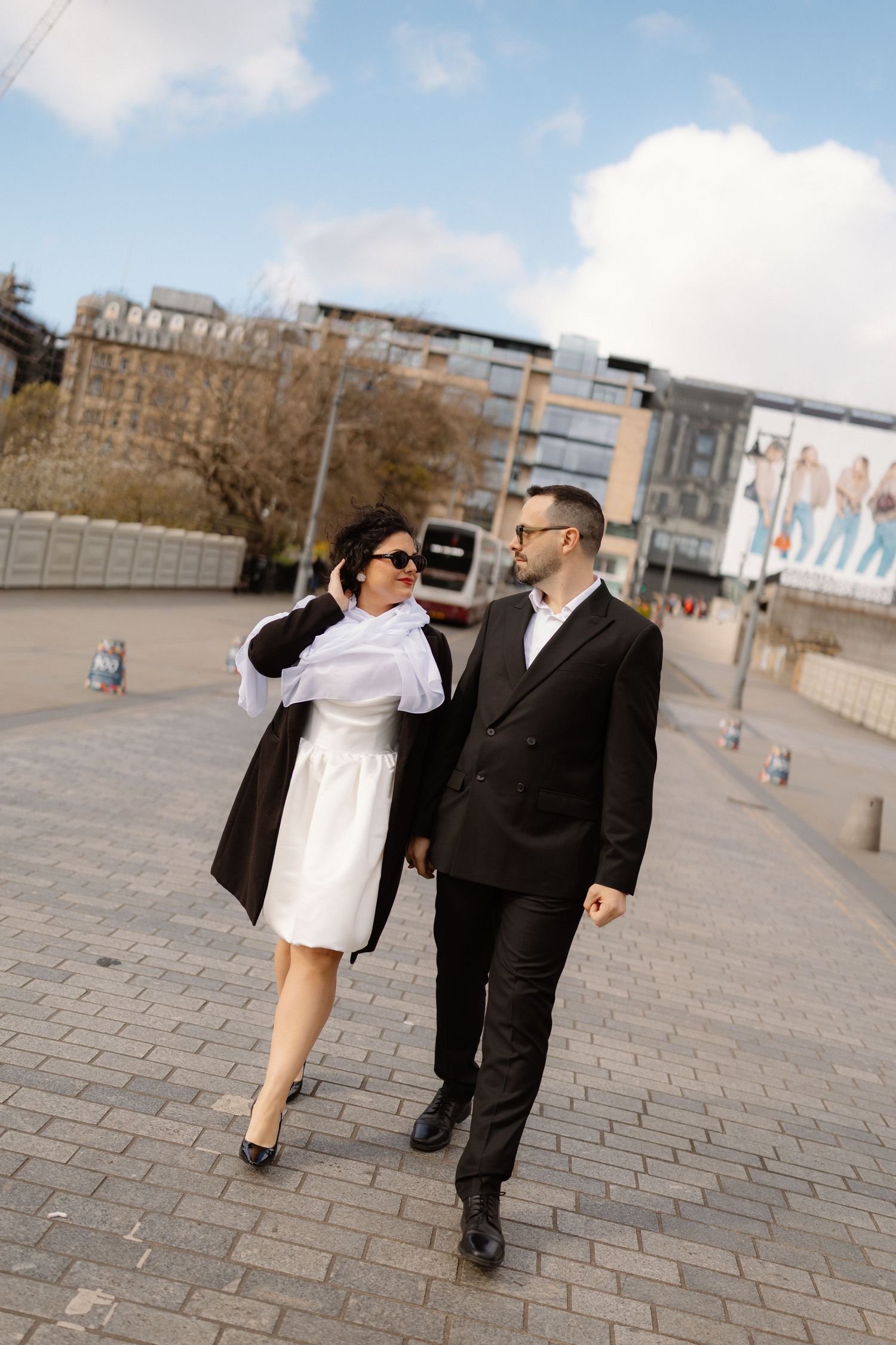 Stylish couple in black and white outfits walking through an urban city square outdoors.