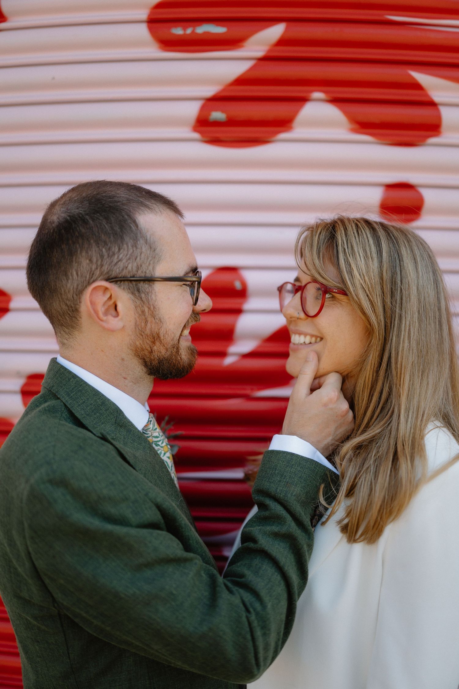 A couple shares an intimate moment in front of a wall with red floral patterns.