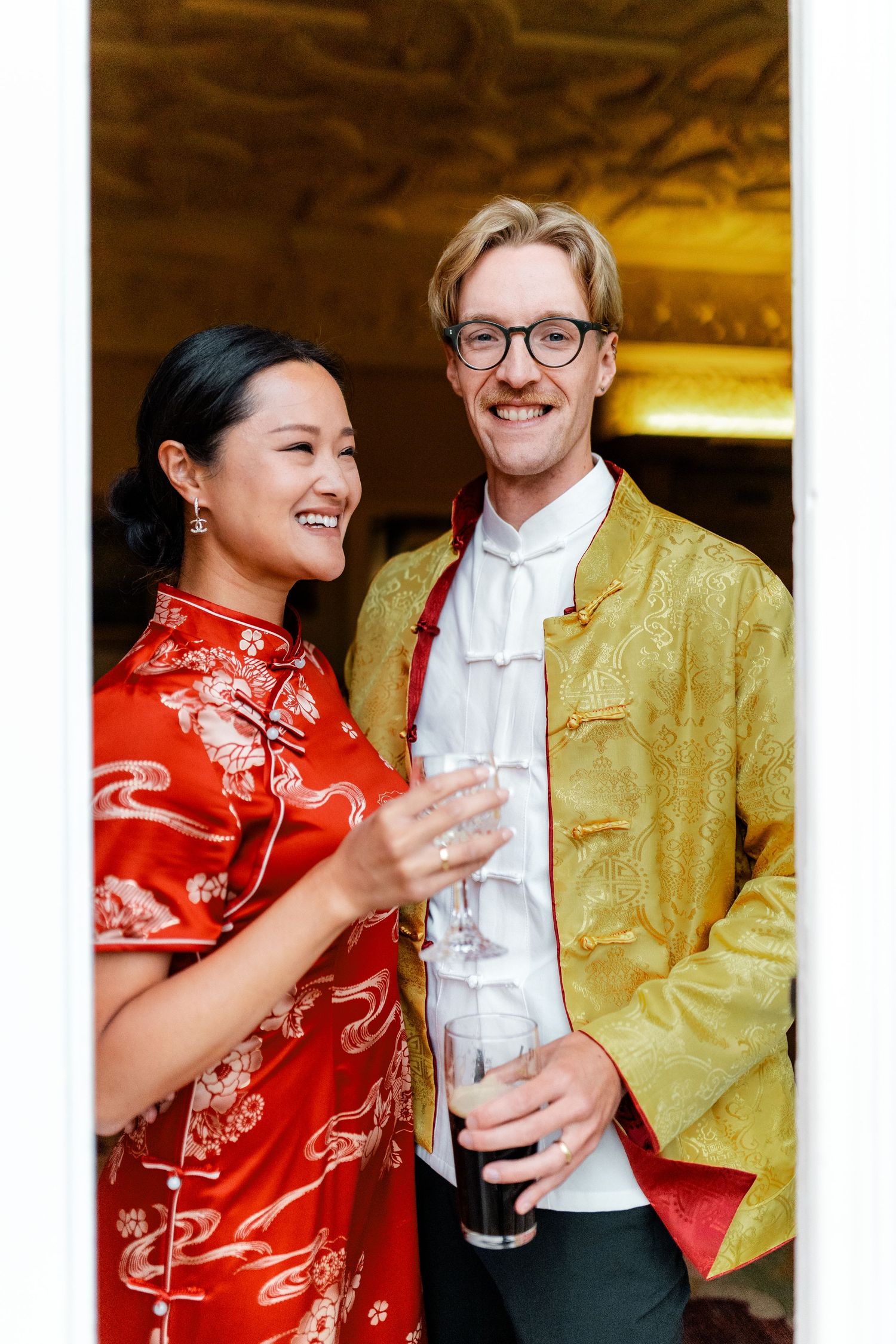 Couple in traditional red qipao and gold formal wear share drinks at a celebration.
