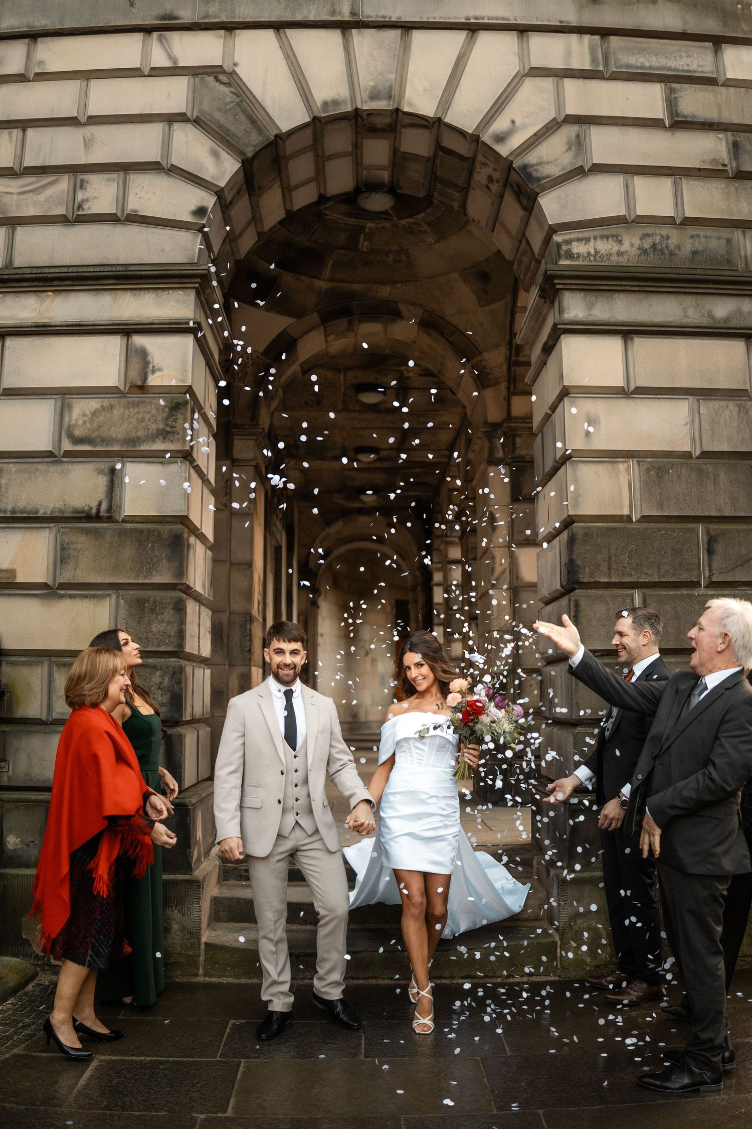 Wedding celebration with confetti under stone archway with fairy lights.