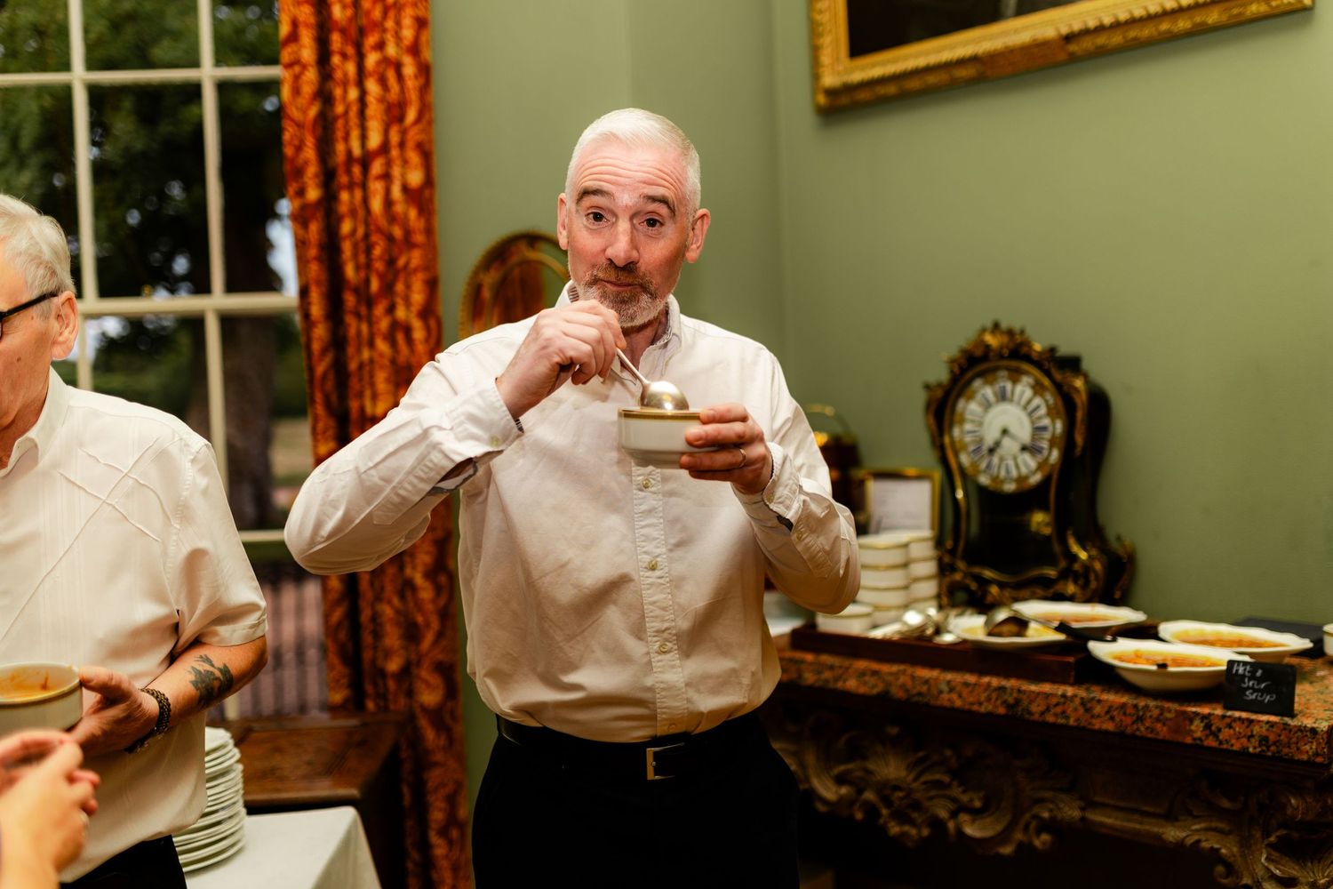 Person sipping from a cup in a room with green walls and floral curtains.