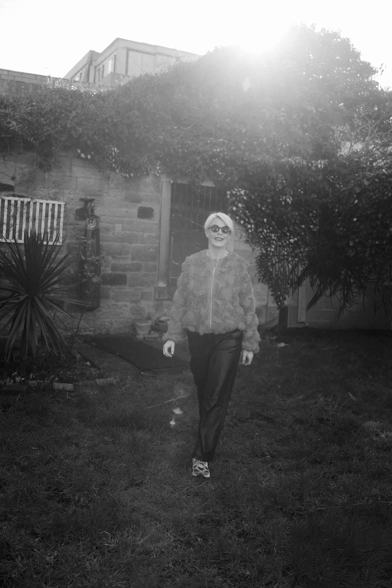 Black and white photo of a person standing in a backyard garden with sunlight streaming through trees.