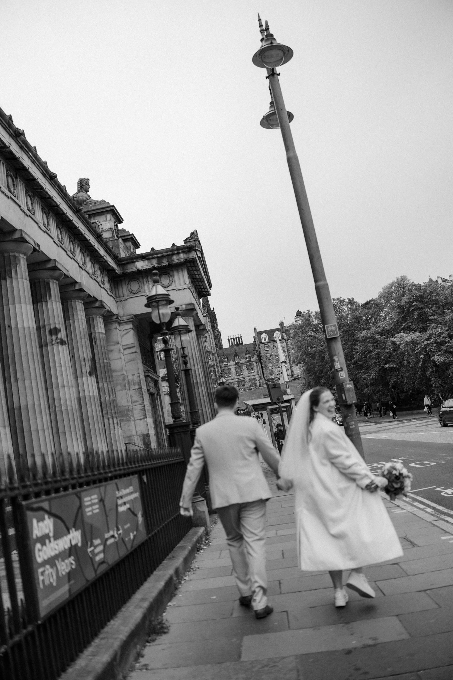 Black and white photo of couple walking along classical architecture street.