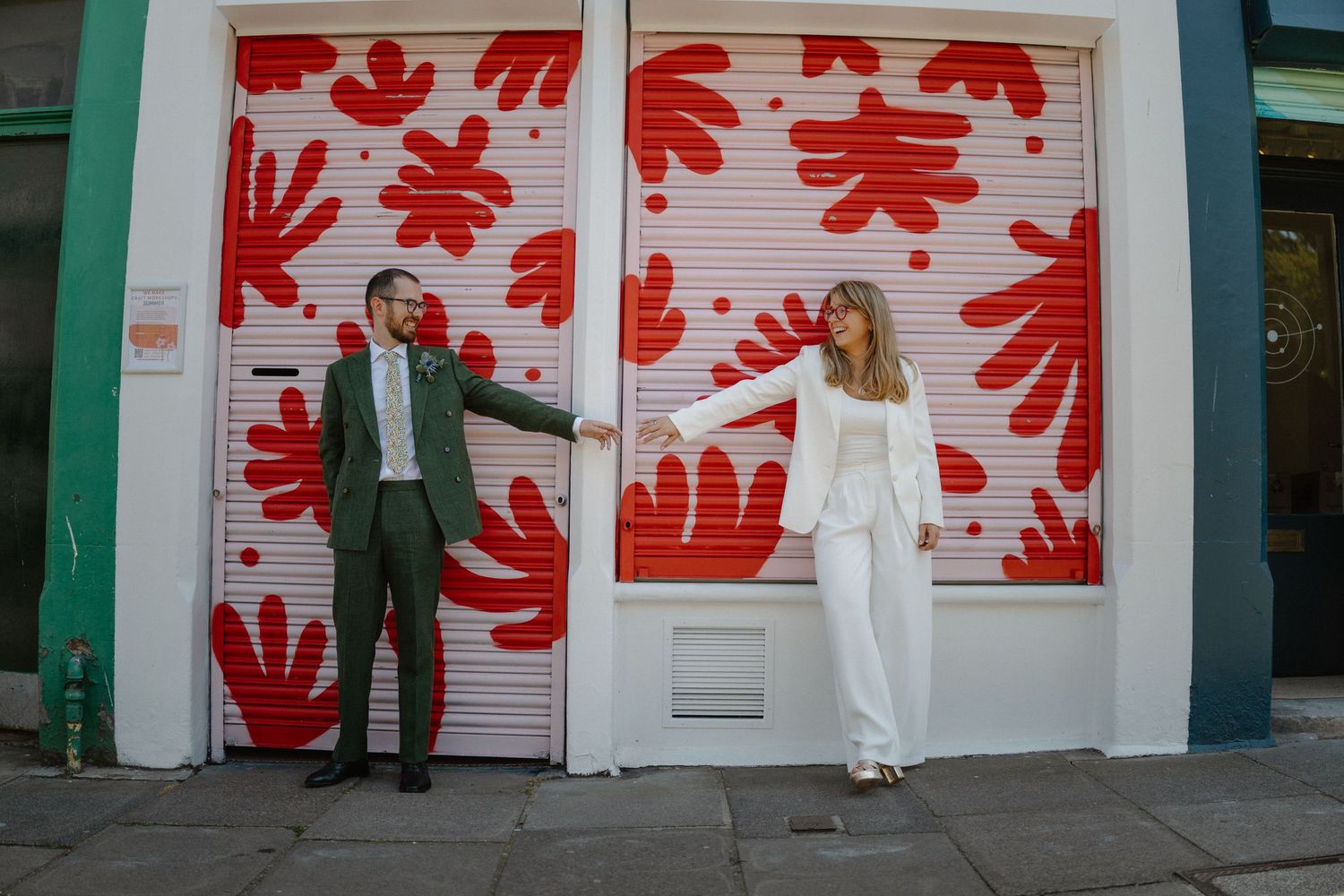 Couple posing playfully against doors with red floral artwork.