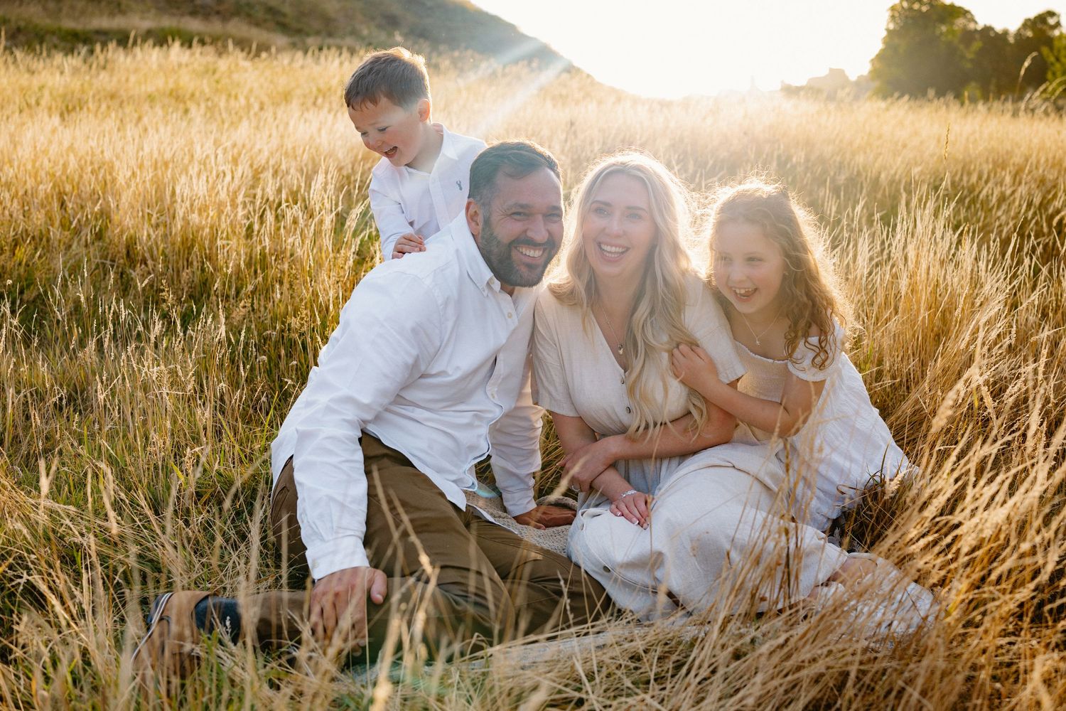 Candid family portrait session in tall grass field during sunset.