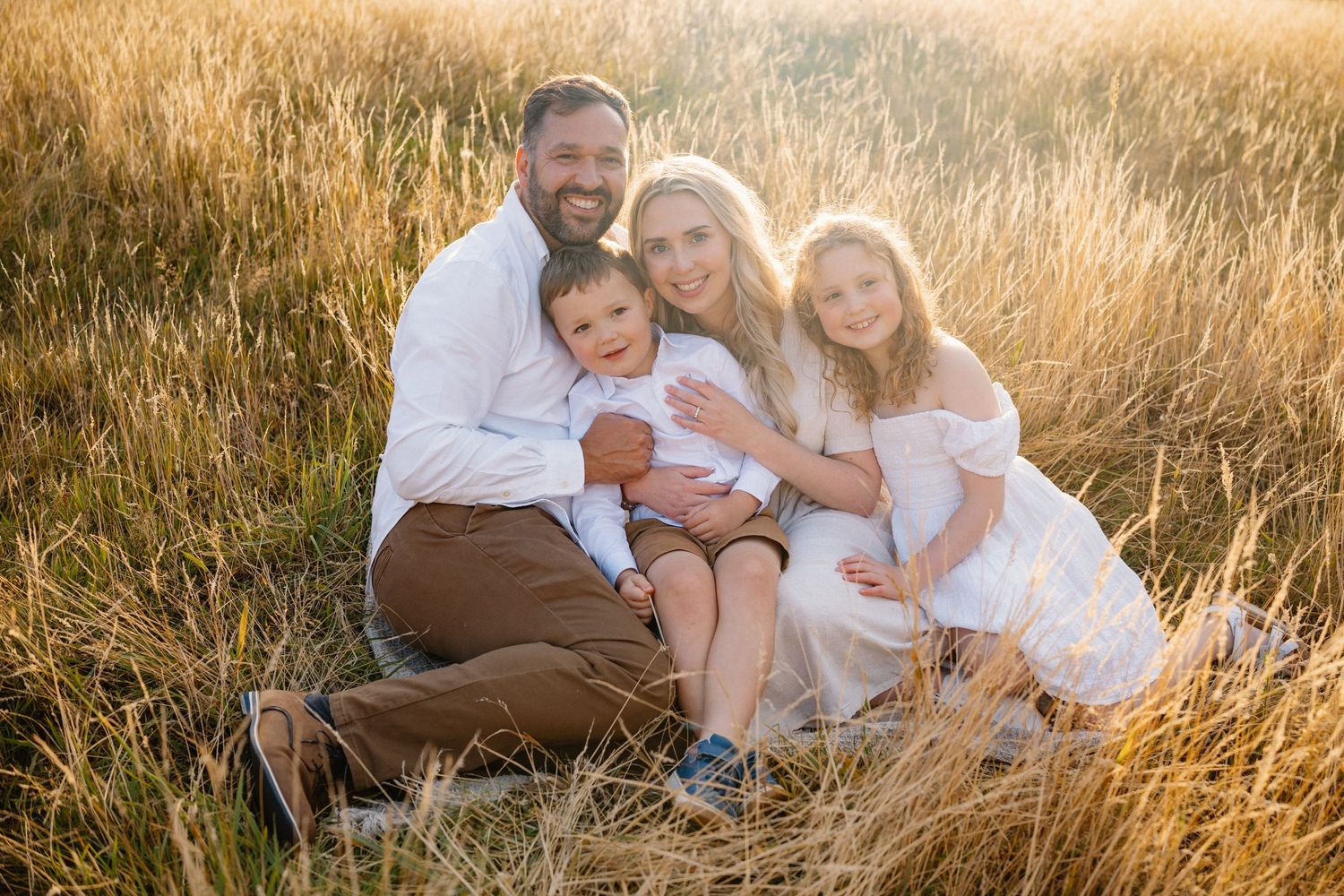 Family relaxes together in tall golden grass during sunset.