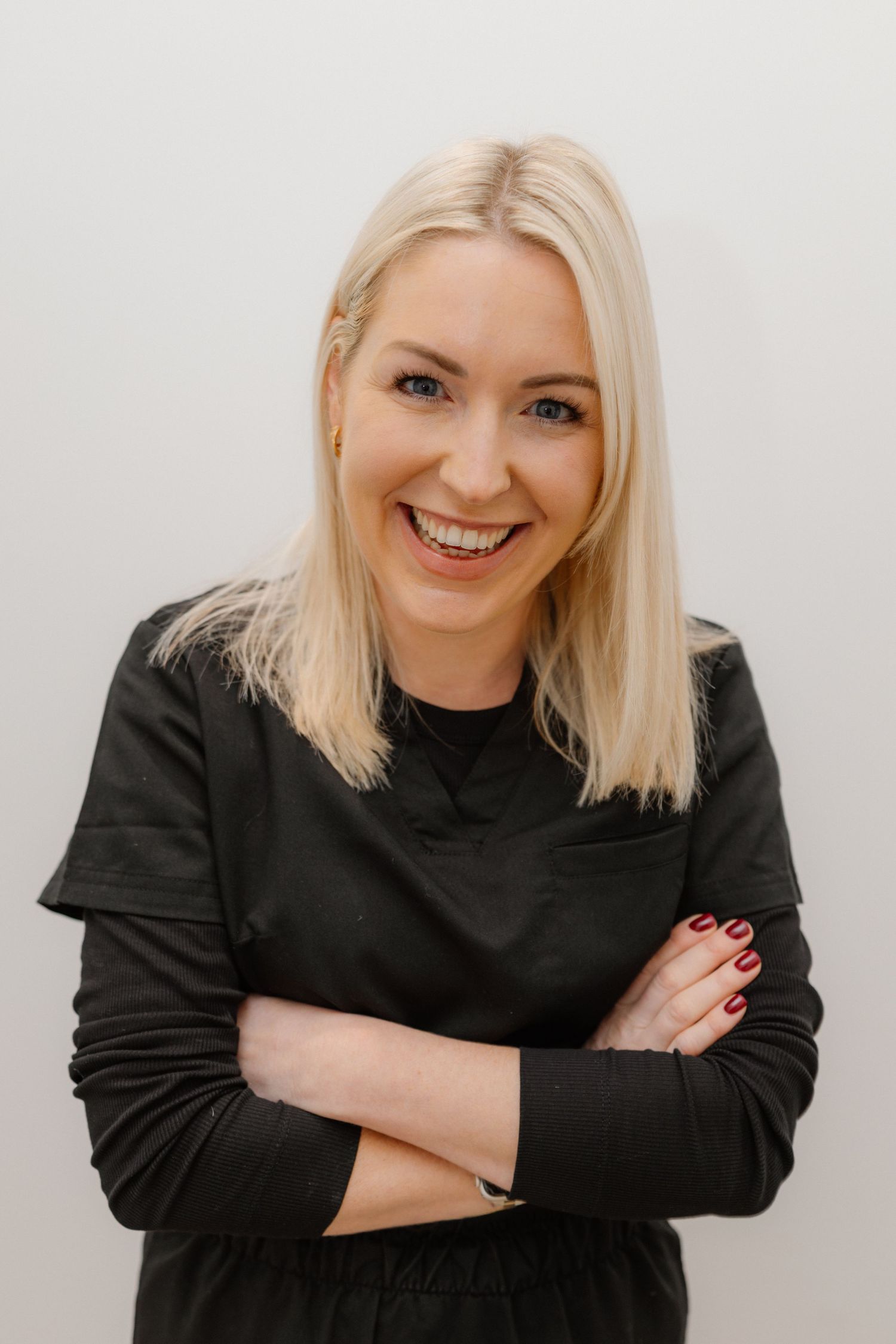 Medical professional in black attire posing with crossed arms in clinical setting.