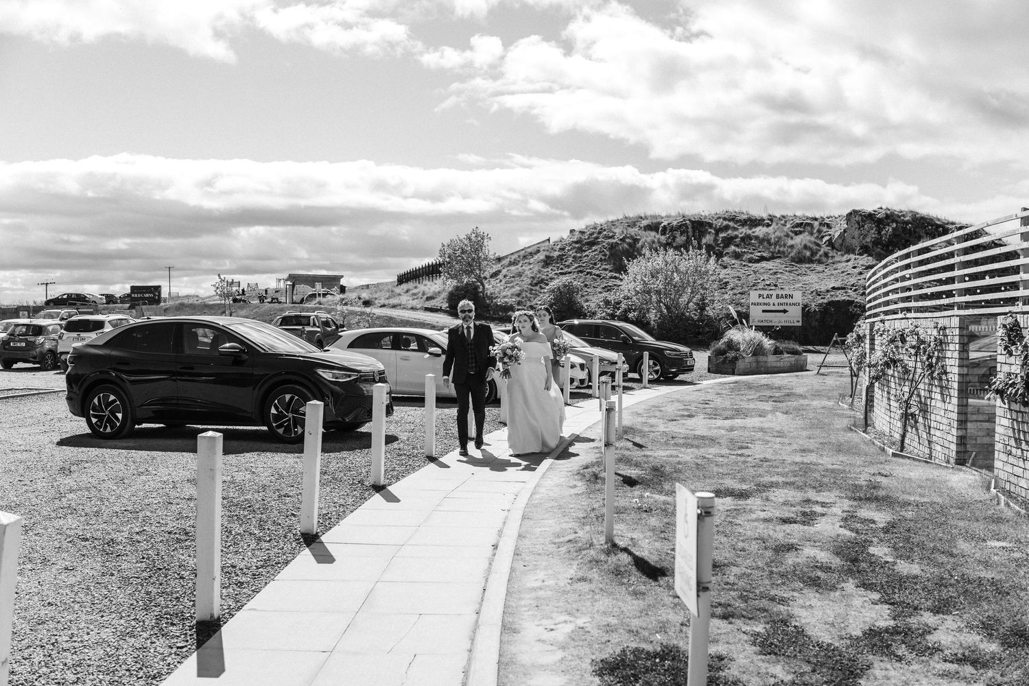 Panoramic view of a coastal wedding venue with cars and guests.