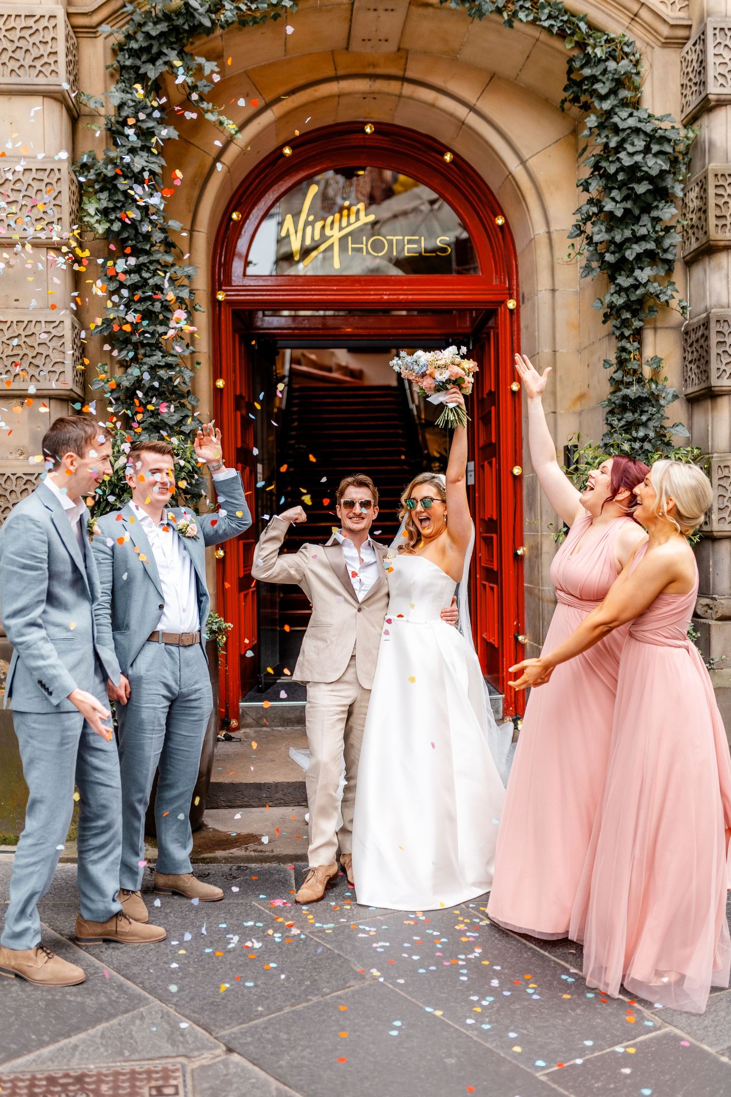 Wedding party celebrates outside decorated venue entrance with pink bridesmaids dresses and confetti.