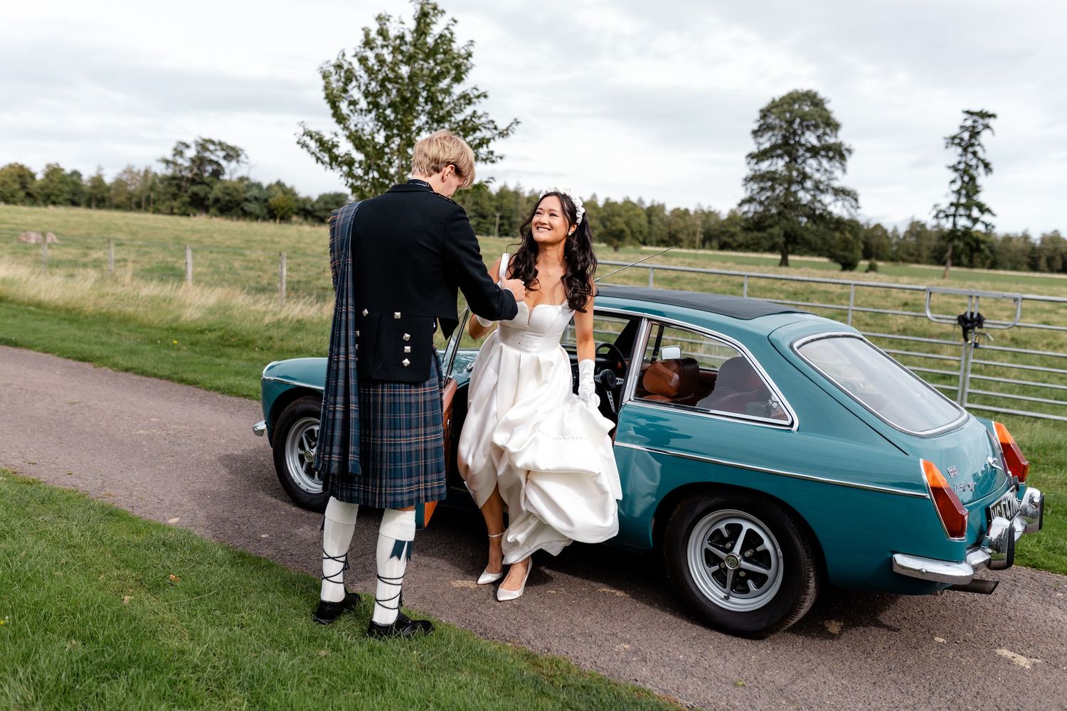 A classic teal MG sports car serves as a wedding getaway vehicle on a country road.