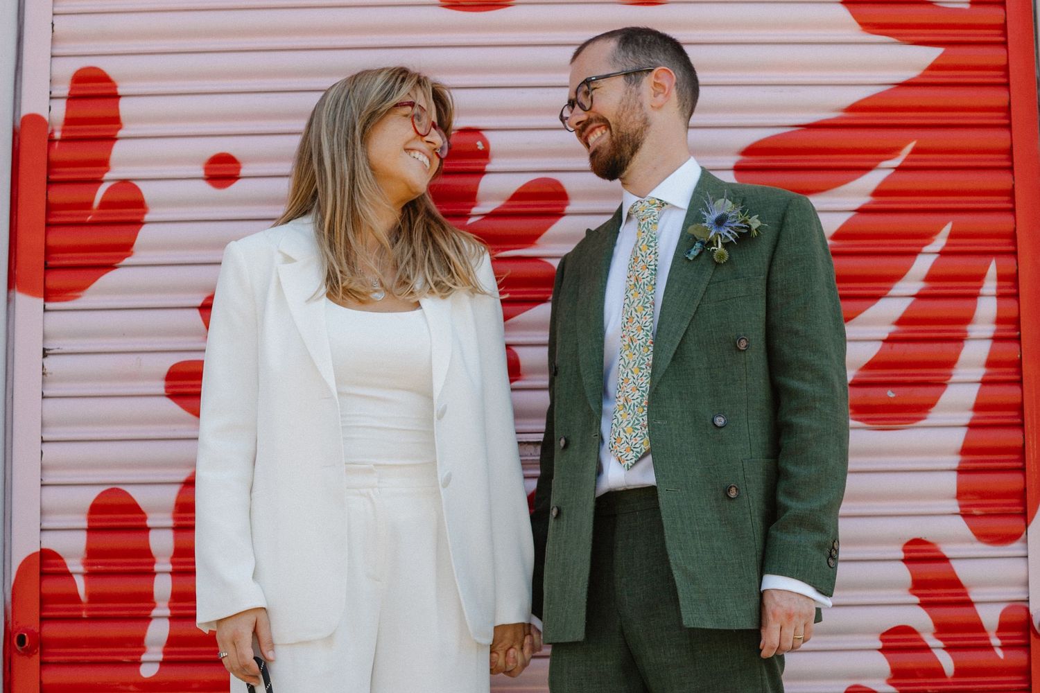 A couple stands together against a wall with vibrant red flower patterns.