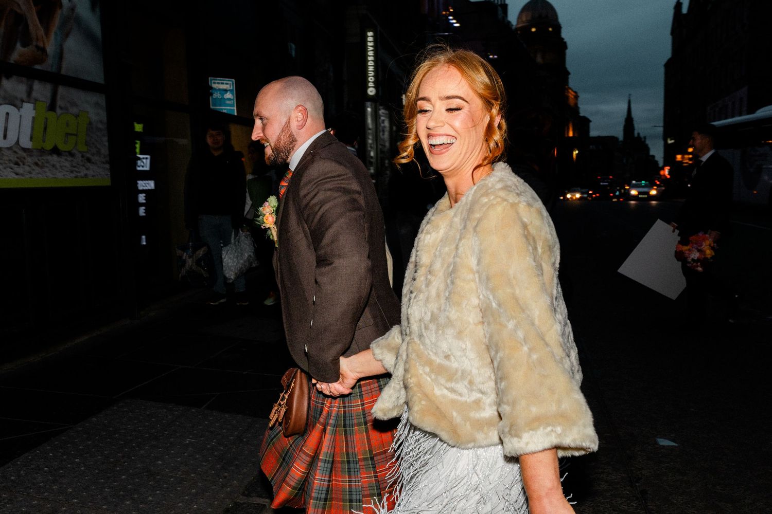 A couple in formal attire walking on a dimly lit street at night.