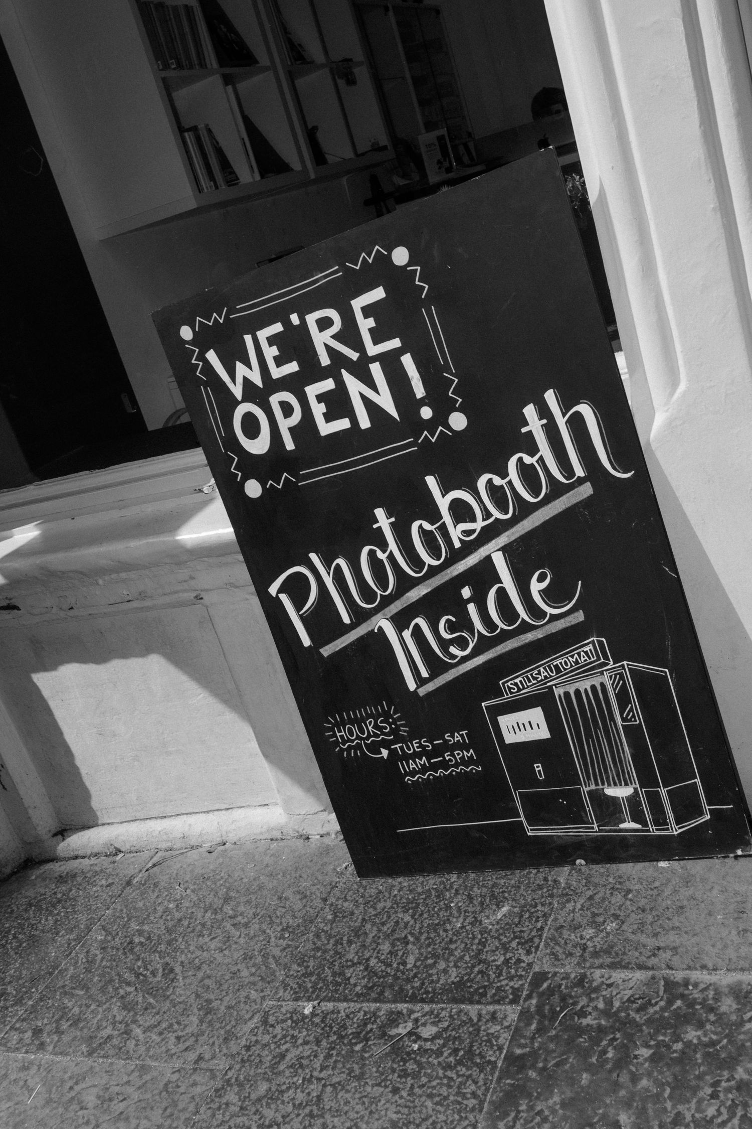 Black and white chalkboard sign reading We're Open with Photobooth Inside and Tuesday-Saturday hours displayed.
