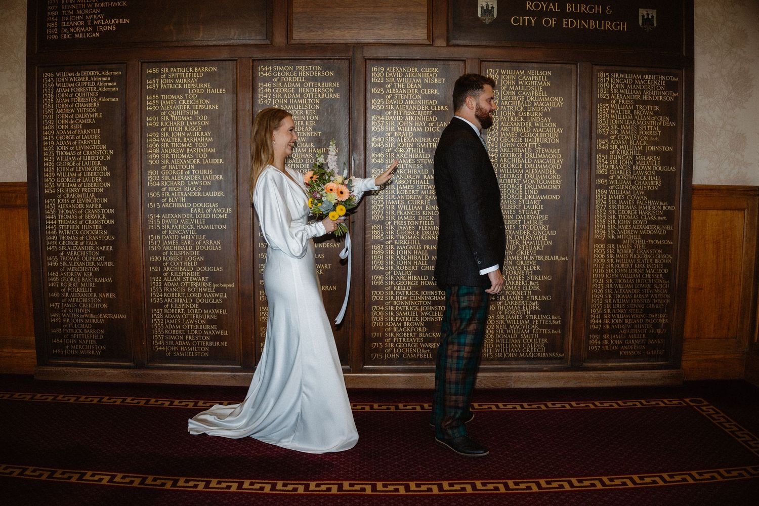 Bride and groom exchange vows in Edinburgh City Chambers with historic honor roll plaques on the wall.