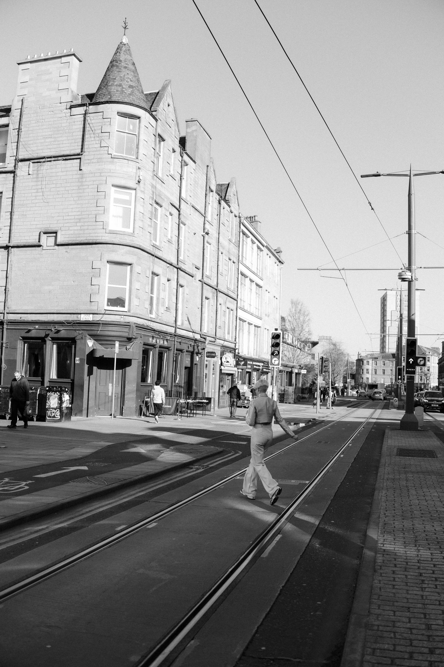A sequence of black and white street photos showing a person crossing tram tracks on an urban sidewalk.