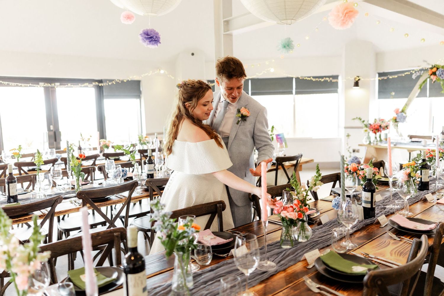 A rustic wedding reception setup with wooden tables and hanging decorations in an airy venue.