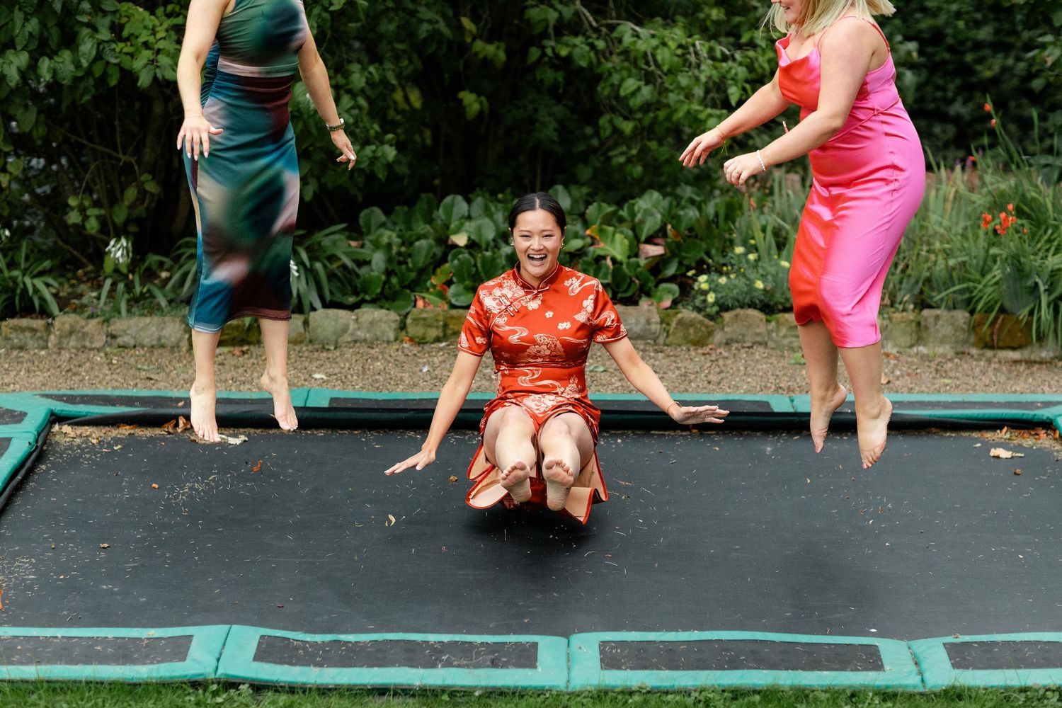 People jumping and playing on a large outdoor trampoline in a garden setting.