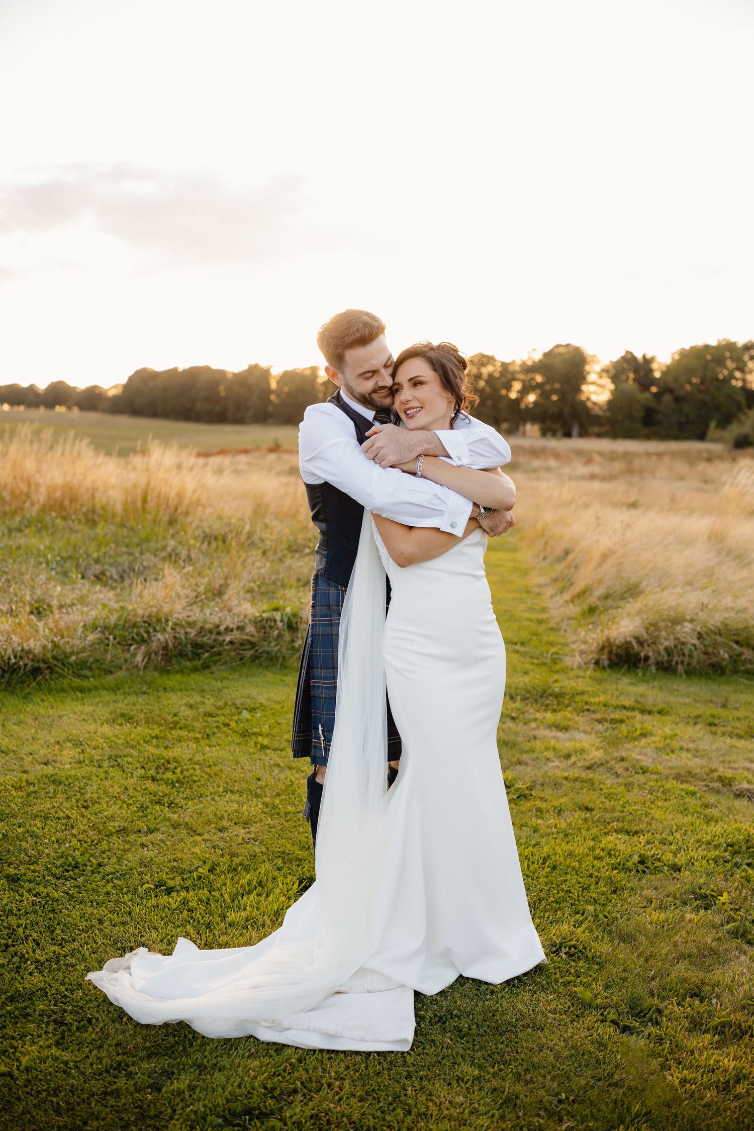 Couple embraces in field during golden hour wedding photography session.