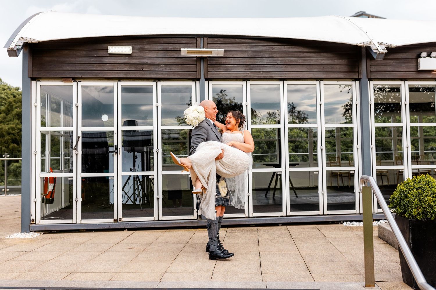 Groom carrying bride, Married couple outside of the Glass House, Edinburgh, Scotland.