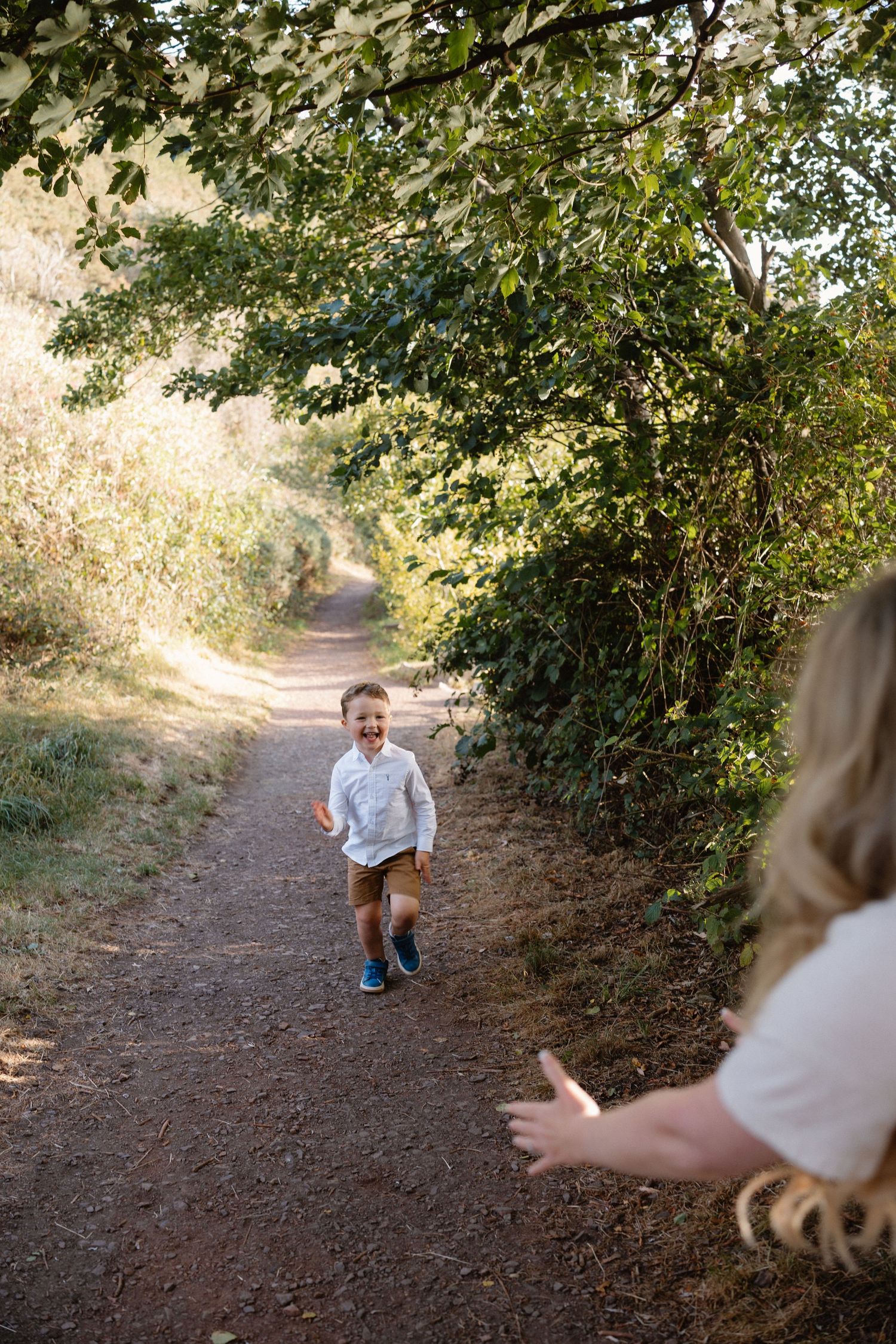 Child runs playfully on a dirt trail through green foliage.