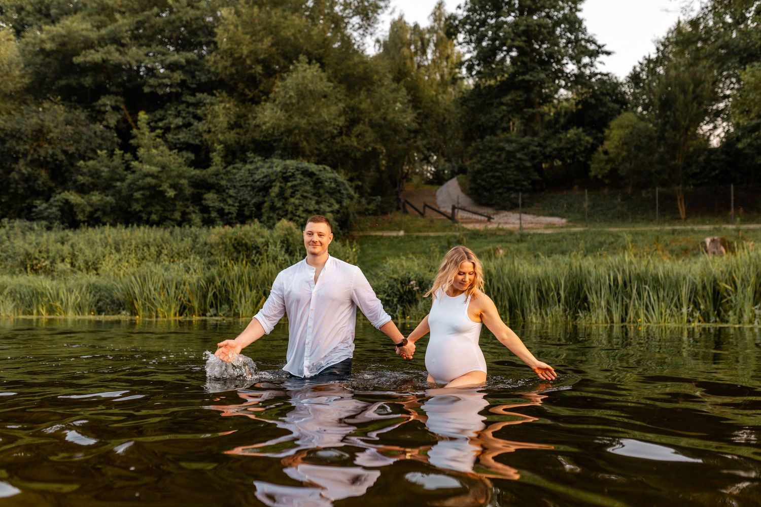 A couple stands in a lake surrounded by greenery during a sunset photoshoot.