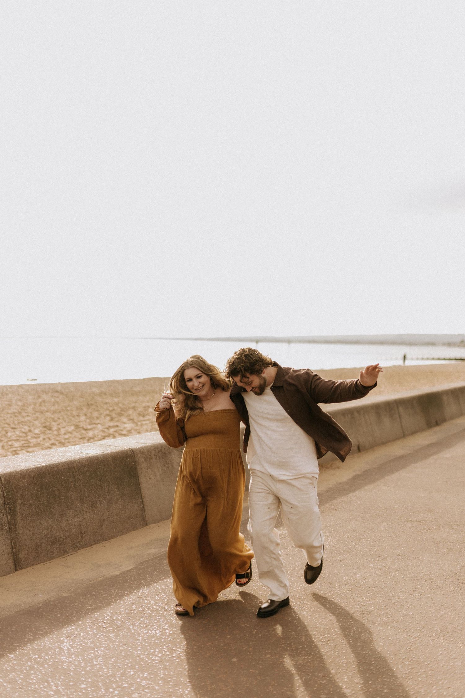 Playful couple walking together along a beachside promenade in casual attire.