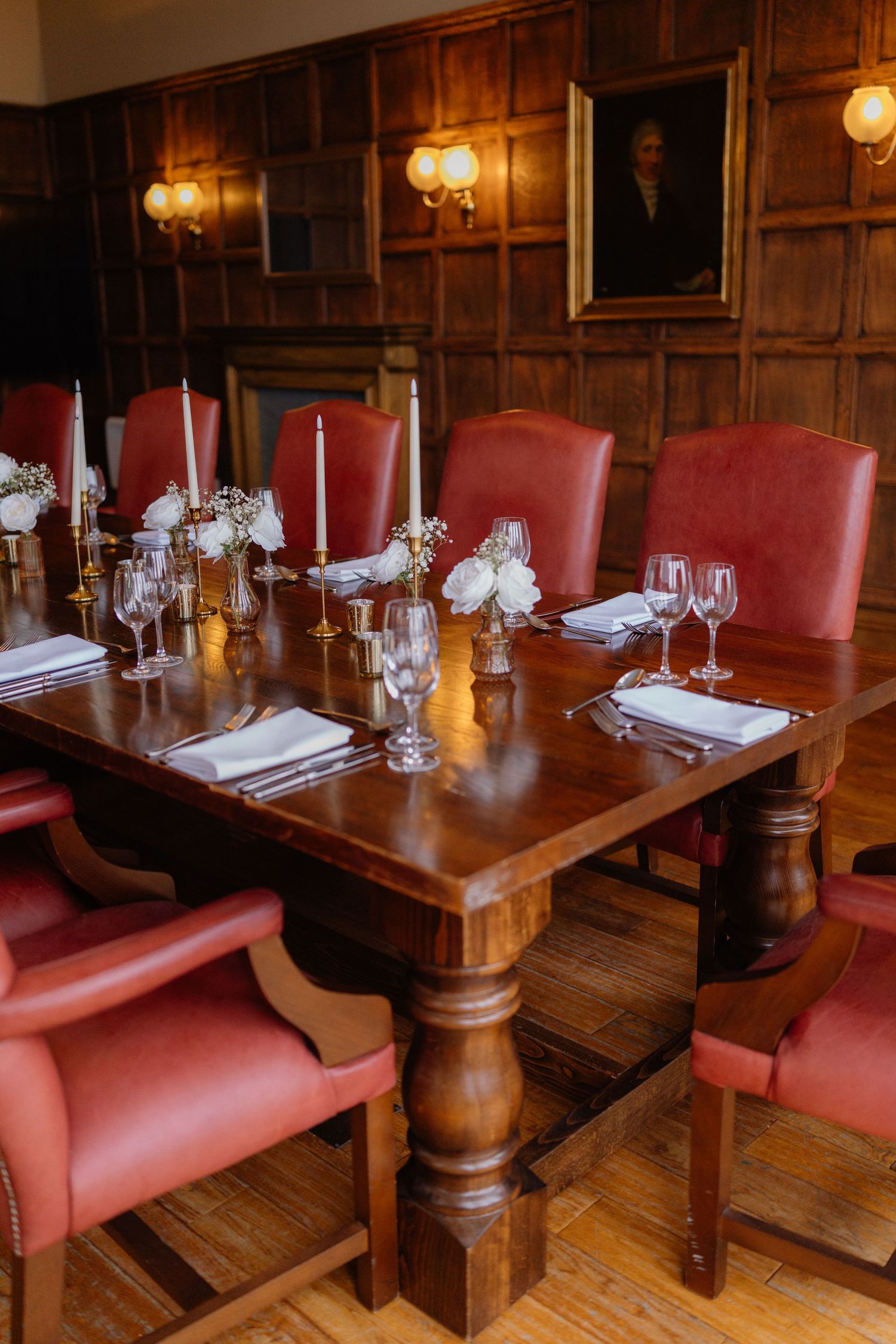 Elegant dining table with red leather chairs and wood paneling in upscale restaurant with vintage wall sconces.