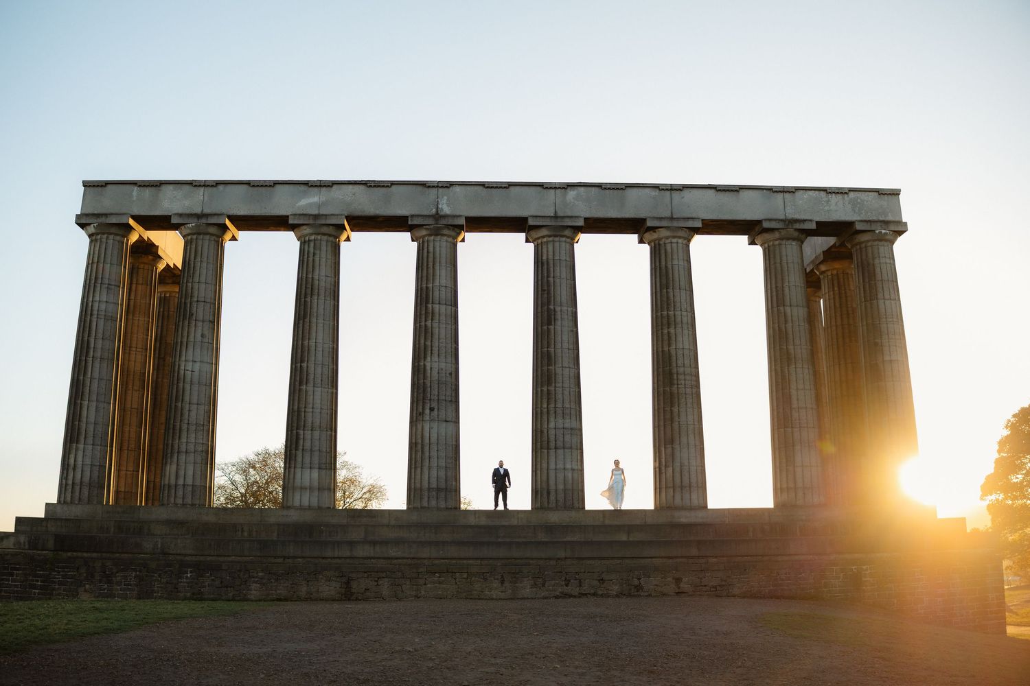 Ancient Greek temple columns silhouetted against dramatic sunset sky.