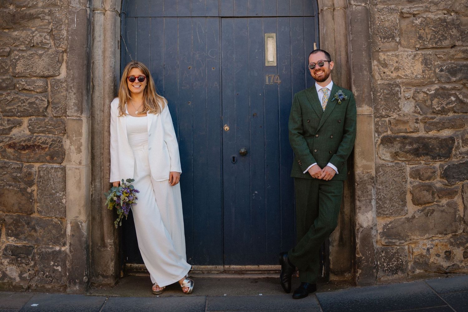 Wedding couple poses against rustic blue door and stone wall exterior.