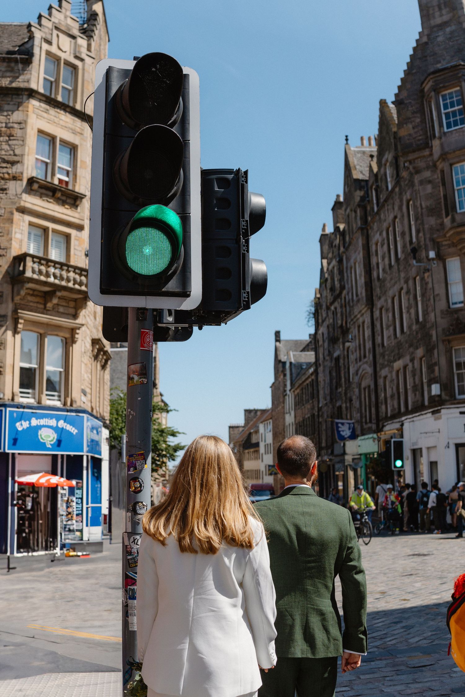 Historic stone buildings line a street with traffic lights and pedestrians in Edinburgh.