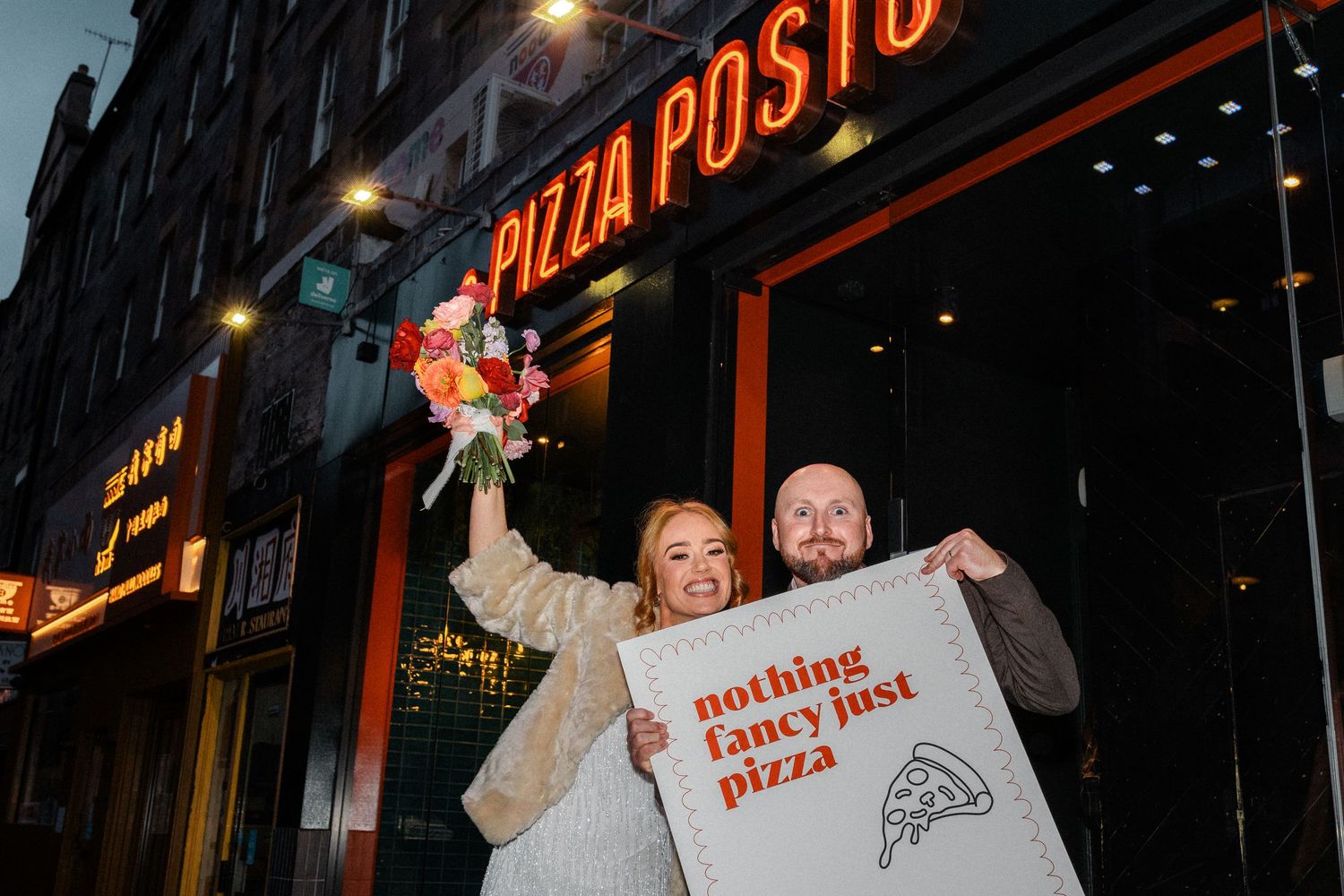 Illuminated Pizza Posto restaurant sign glows in red neon against dark city street at night.