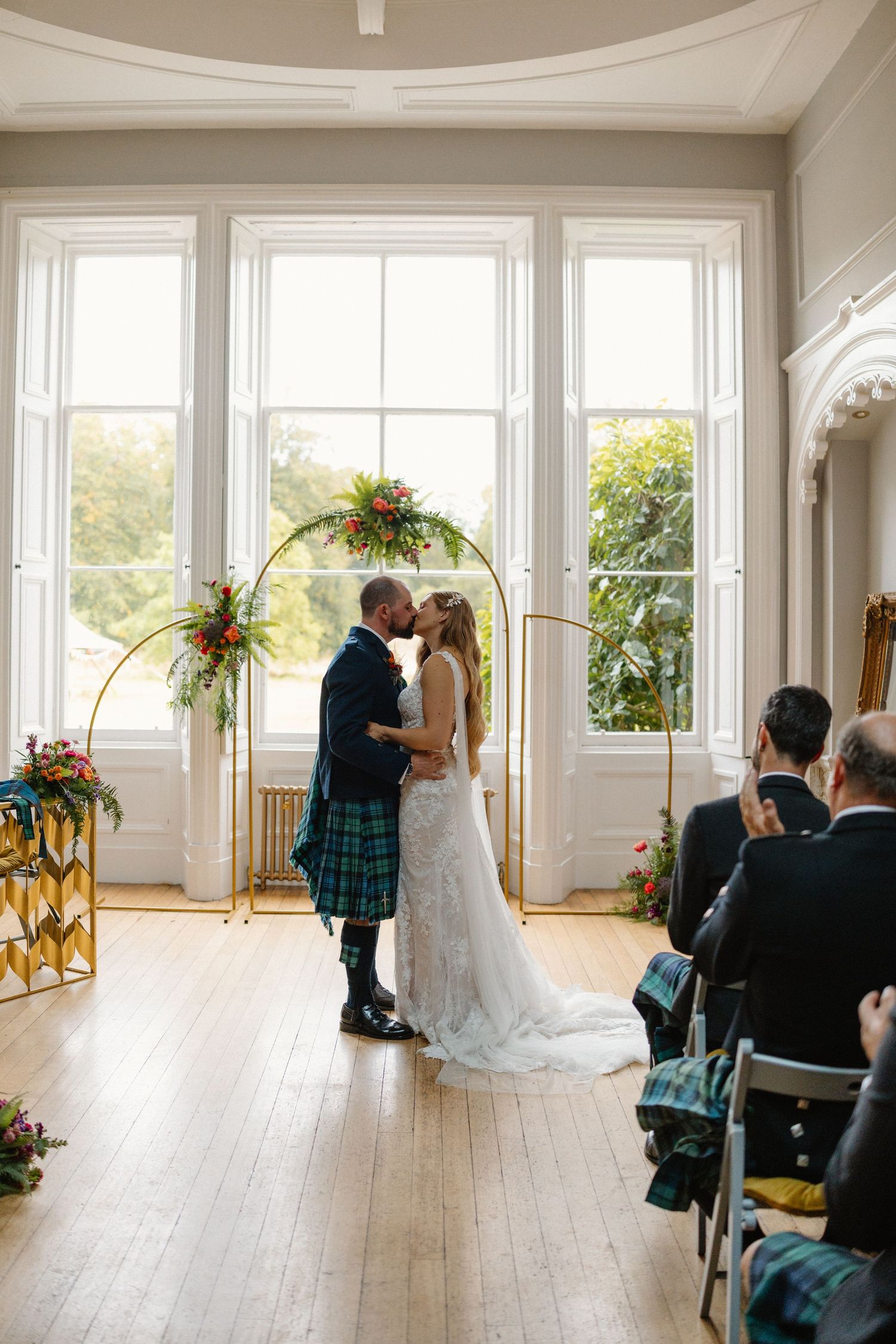 Wedding ceremony setup in a bright room with gold arches and floral decorations.