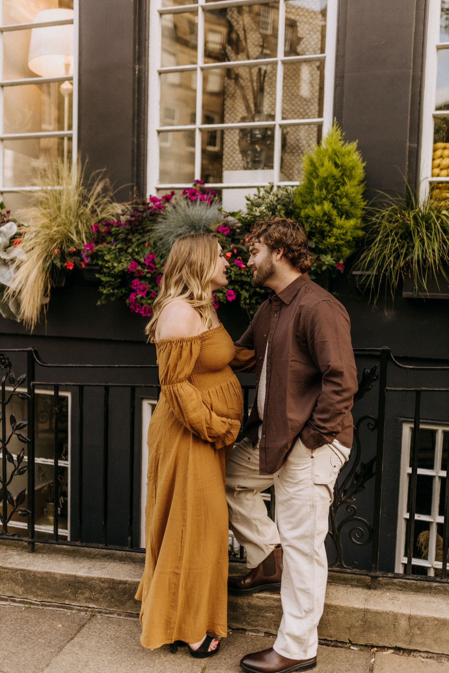 A couple shares an intimate moment outside a shop with flower boxes and greenery.