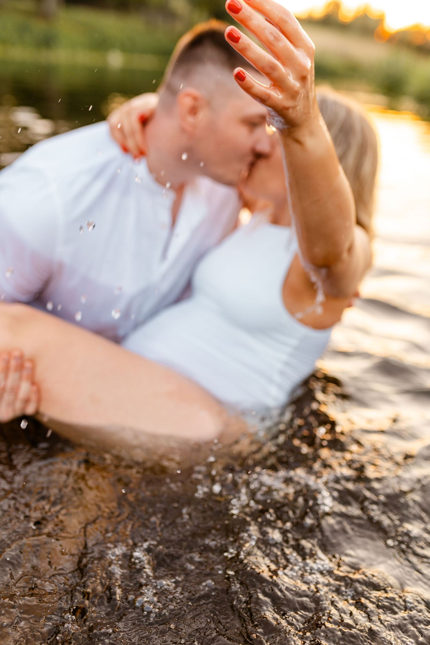 Water splashes around a couple during an intimate moment at golden hour.