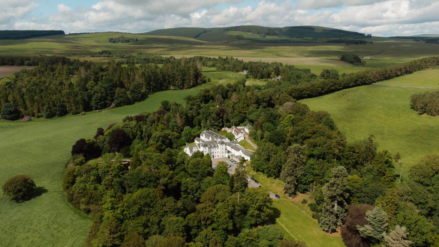 Aerial view of a grand country estate surrounded by lush green trees and rolling hills in Scotland.