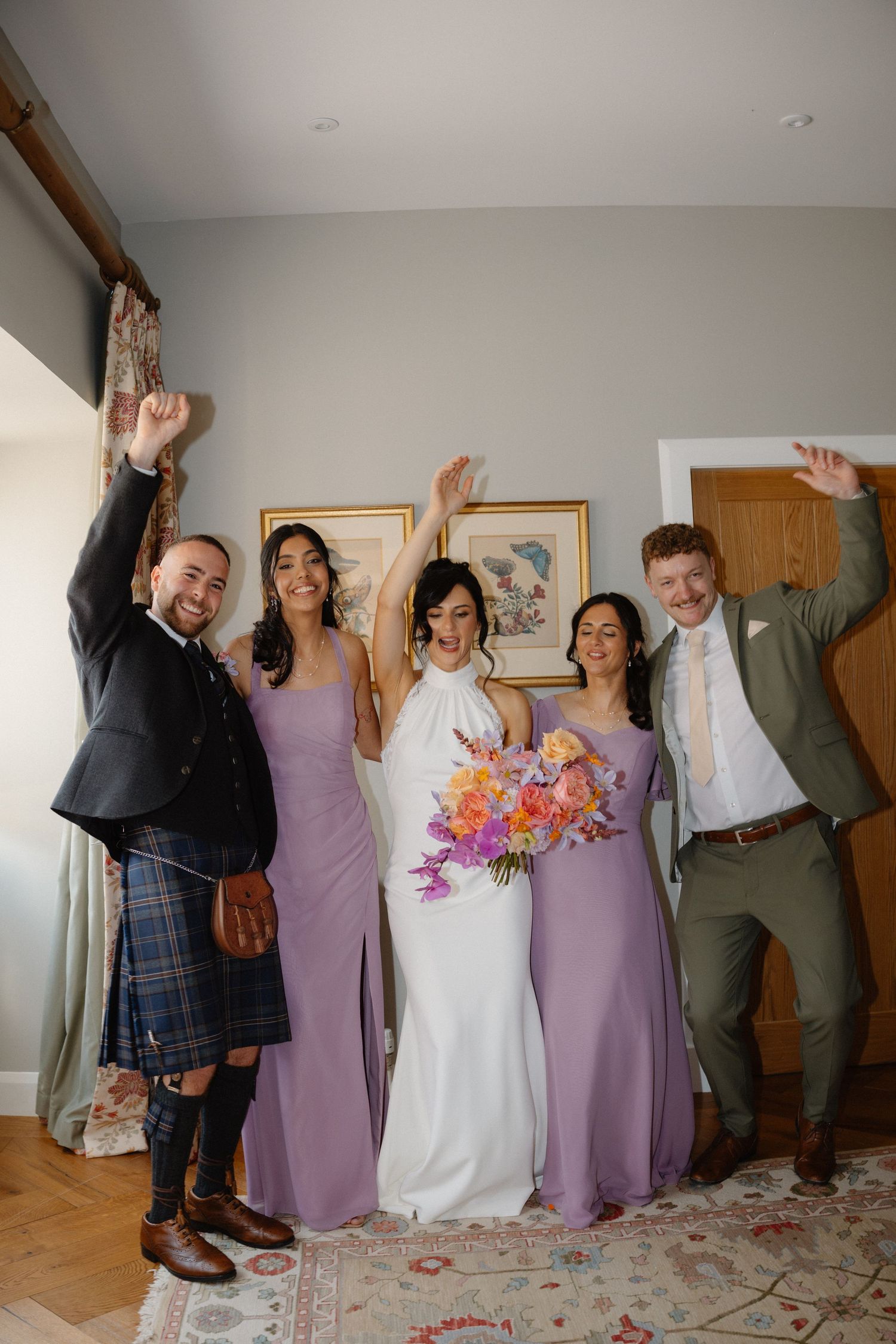 Bride in white gown with bridesmaids in lavender dresses and groomsmen celebrating joyfully.