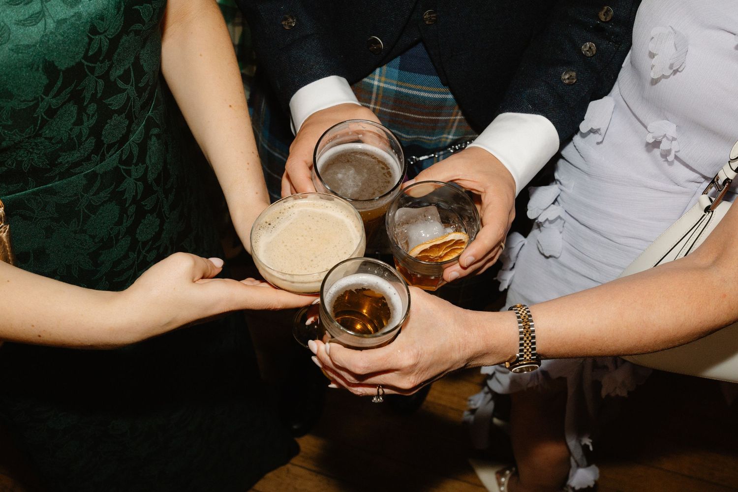 Wedding guests clink glasses of beer and whisky in a celebratory toast at reception.