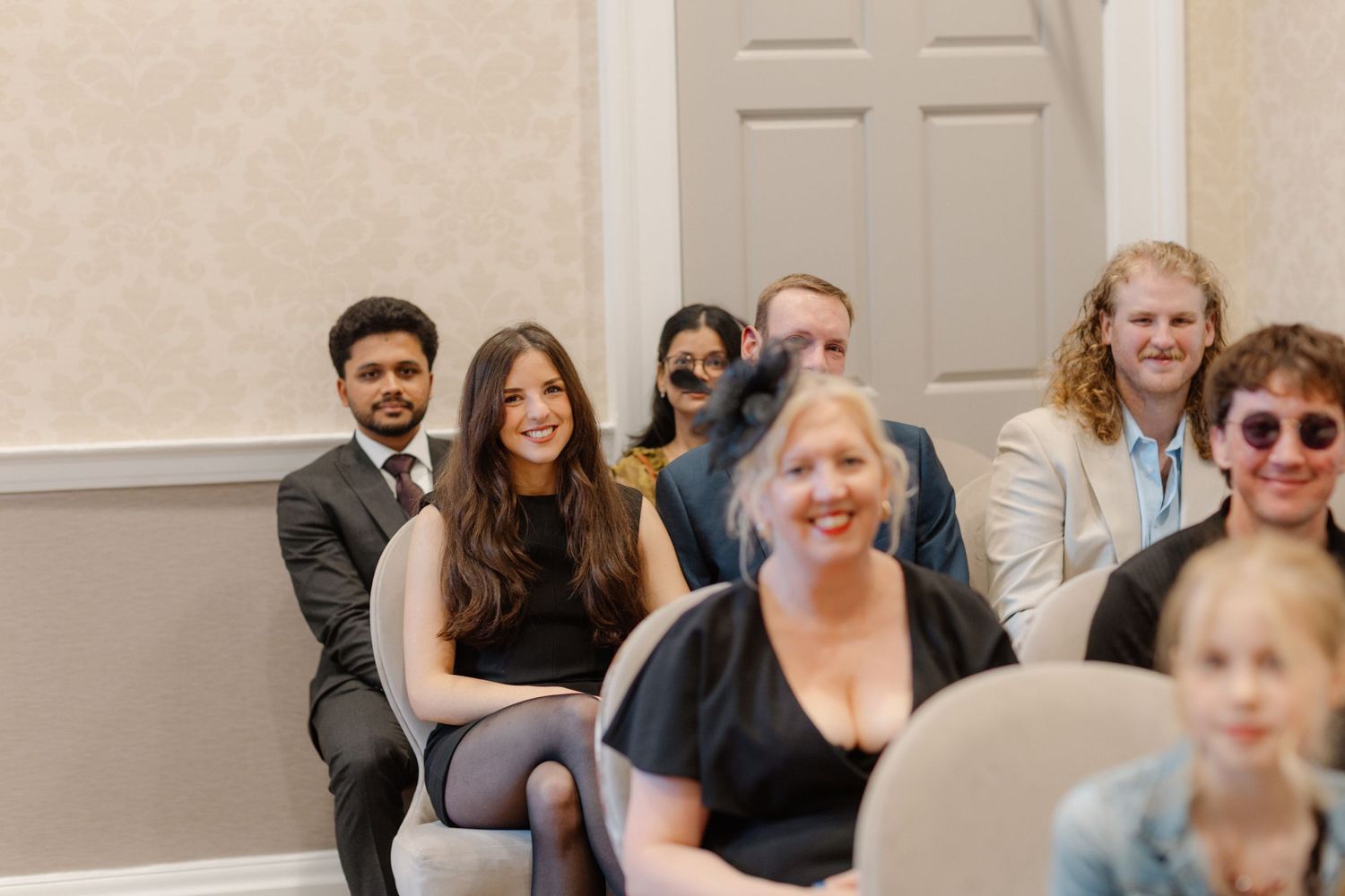Smiling wedding guests seated in rows at an elegant indoor ceremony venue.